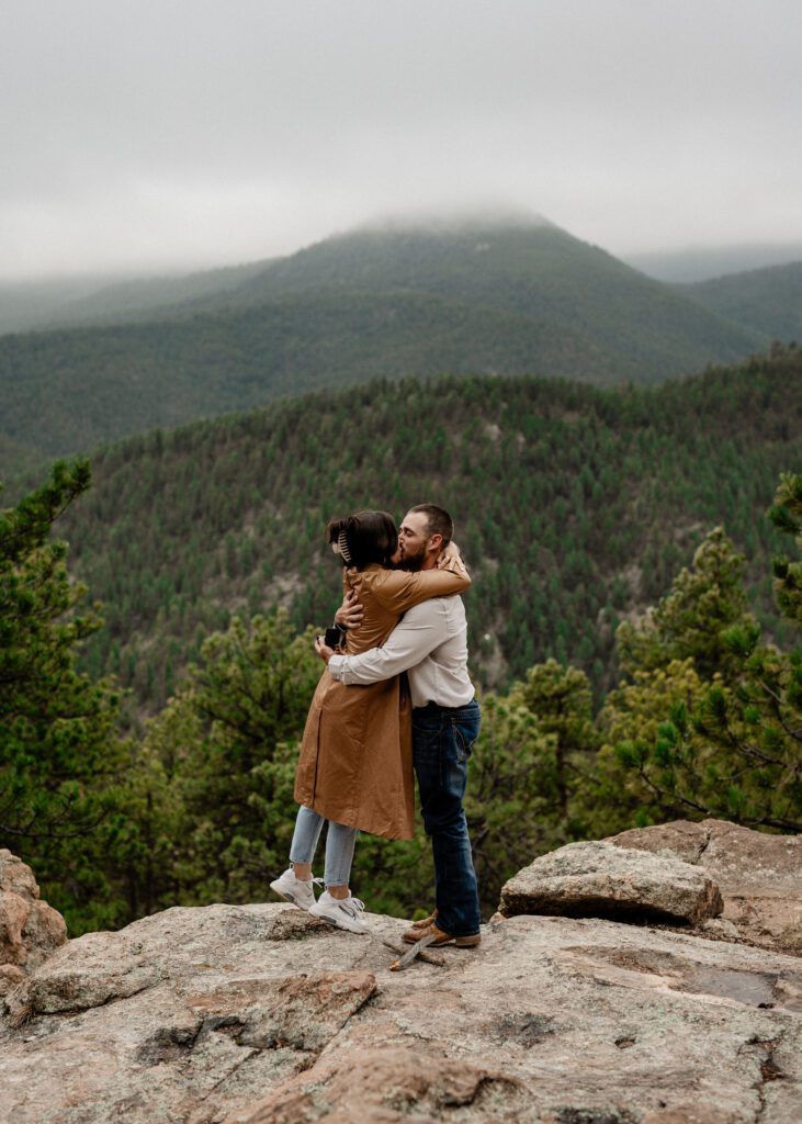 boyfriend and girlfriend hugging and kissing on the side of a mountain after he just proposed to her in Colorado