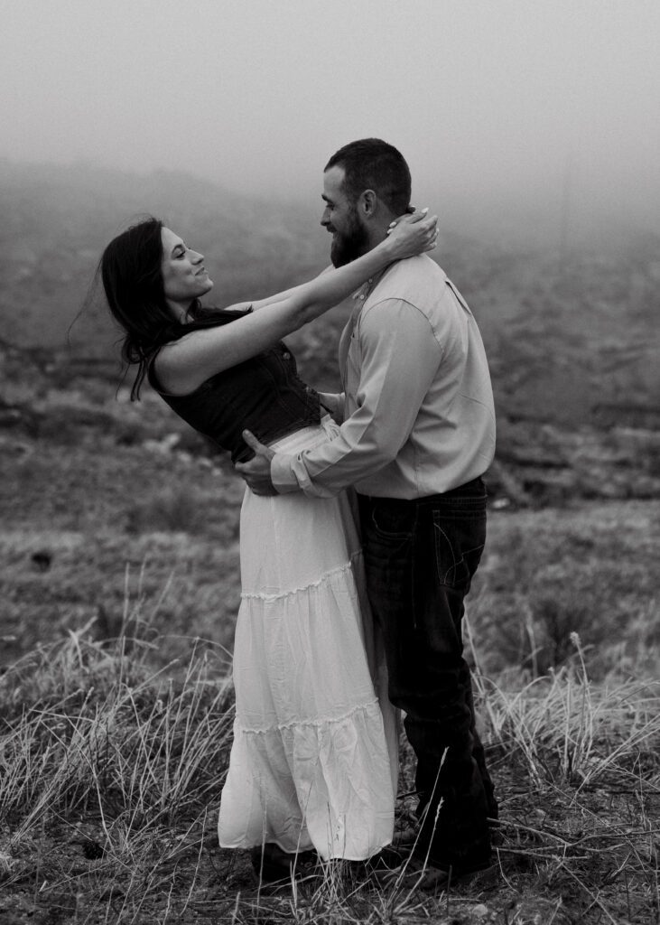 fiancee holding her mans neck while she leans back and smiles at him in a misty field during their proposal in colorado