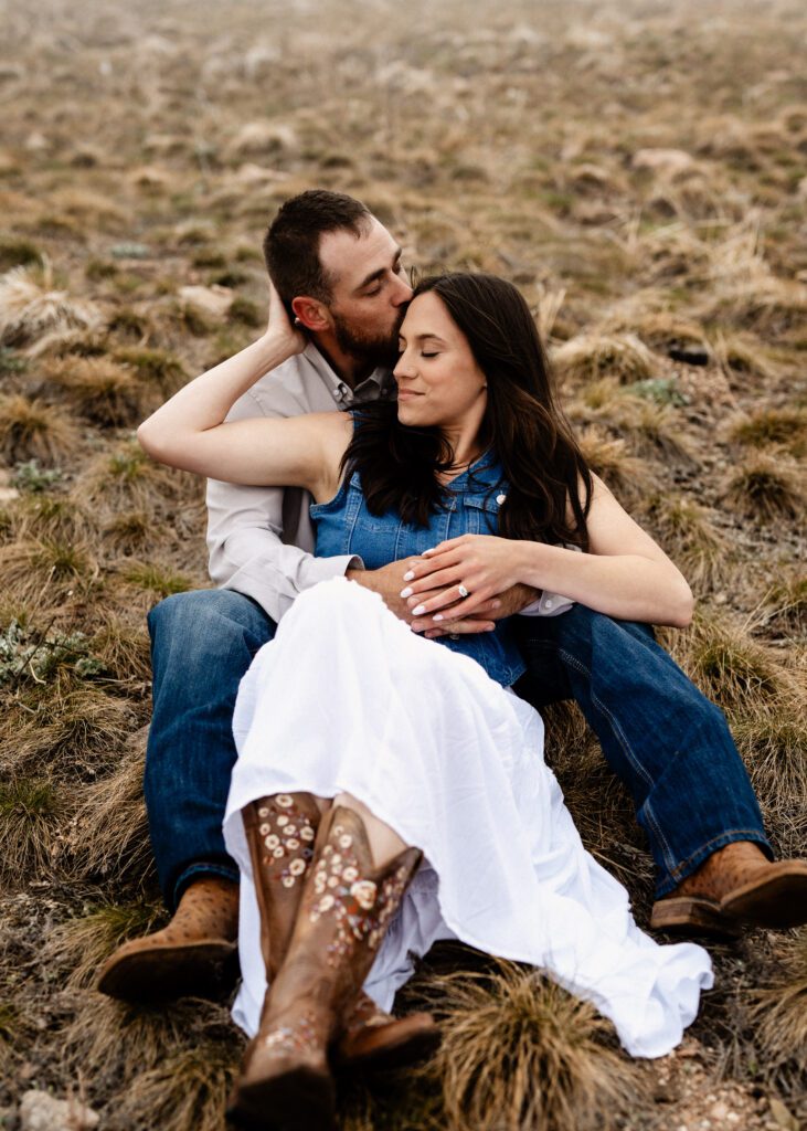 cute newly engaged couple sitting in a field together kissing during their colorado engagement session