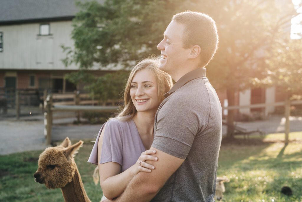 cute couple laughing together while the sun shines behind them during their couples photoshoot at an alpaca farm