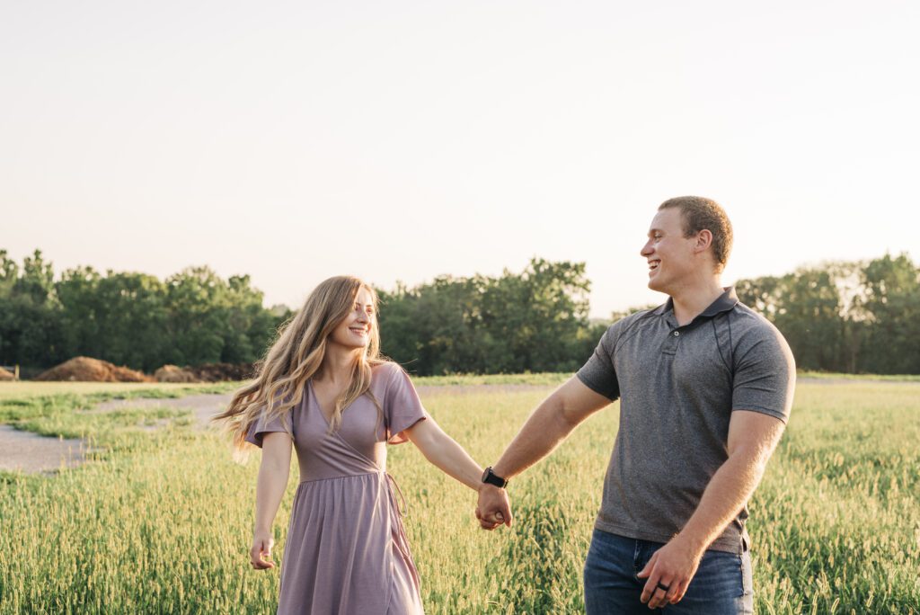 couple holding hands and walking through a field together during their couples session