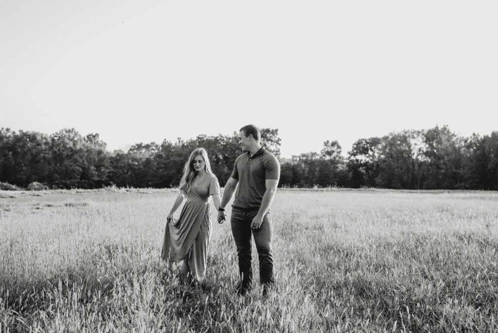 couple walking through a field together holding hands during their couples engagement session