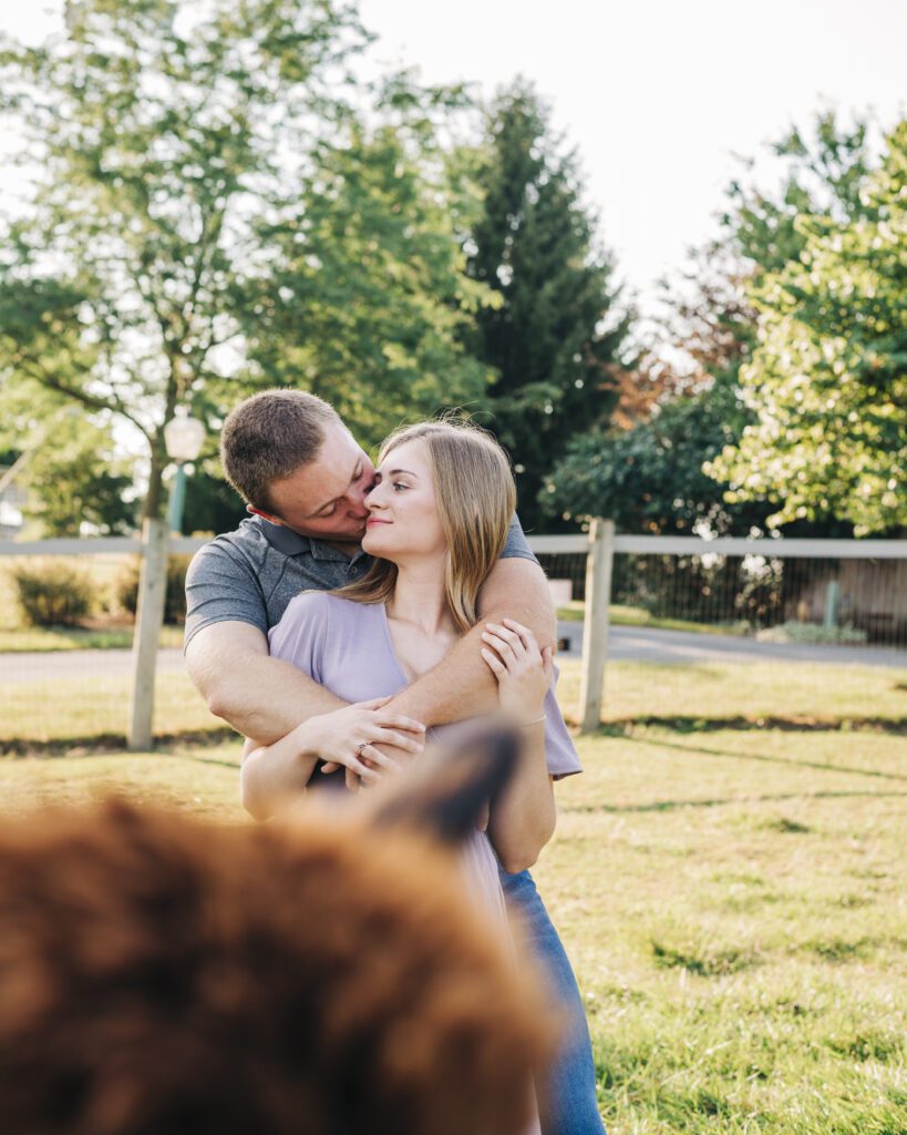 boyfriend kissing his girlfriend as an alpaca photobombs the picture during their couples photoshoot at an alpaca farm