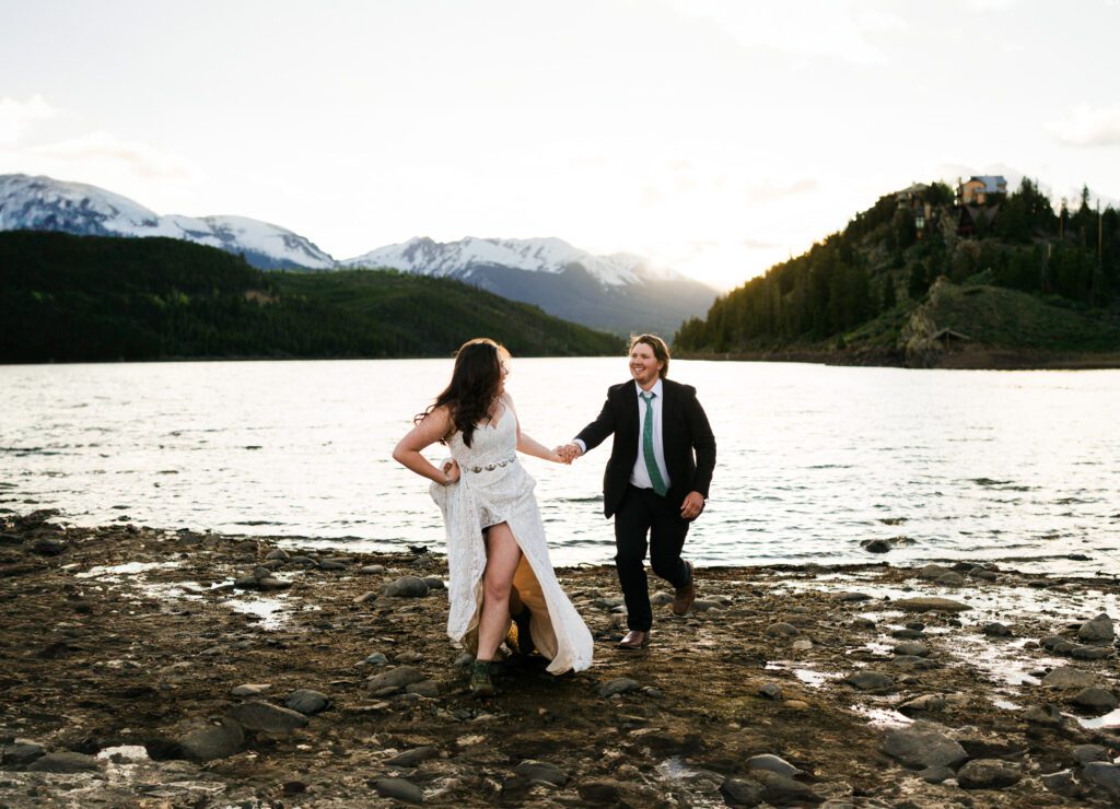 bride and groom holding hands and running towards the camera with the mountains in the background during their Colorado Elopement at Sapphire Point Overlook