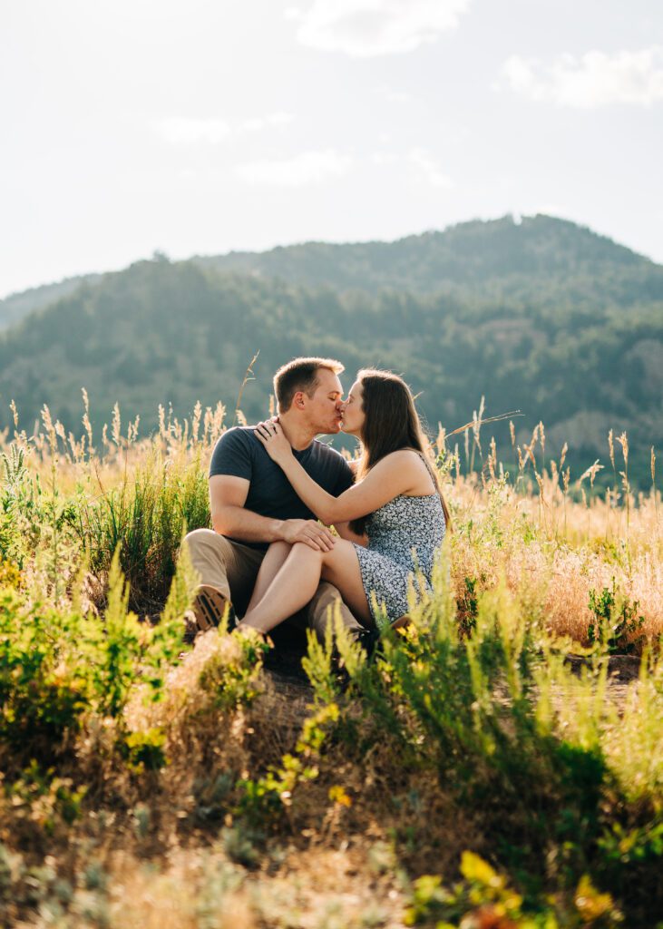 engaged couple kissing while sitting in a meadow at sunset during their boulder engagement photos