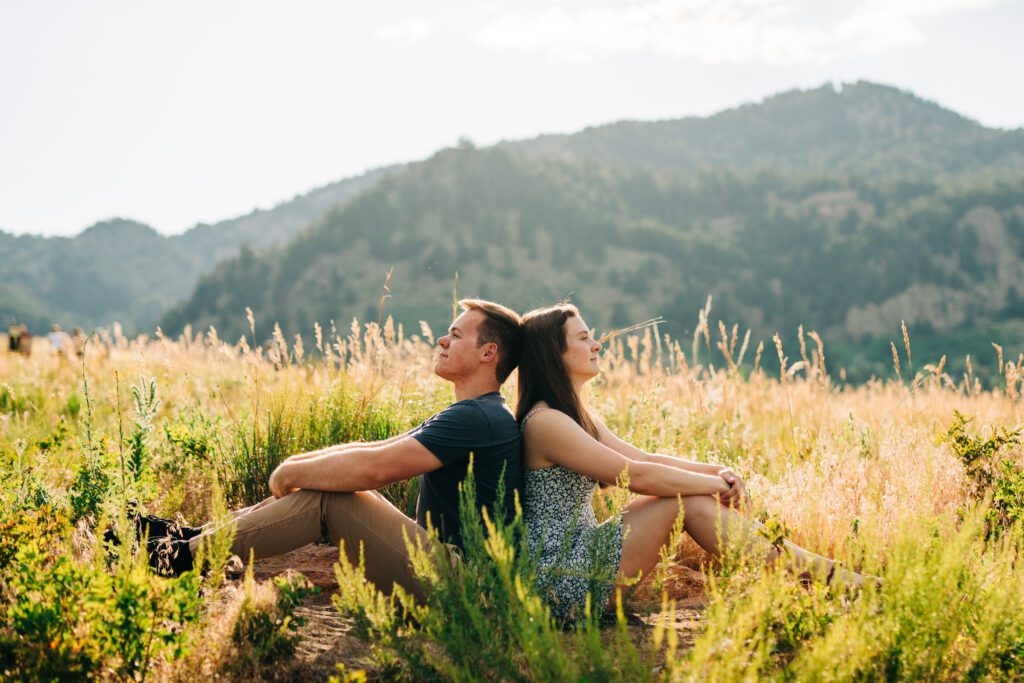 engaged couple sitting back to back in a meadow during their boulder colorado engagement session
