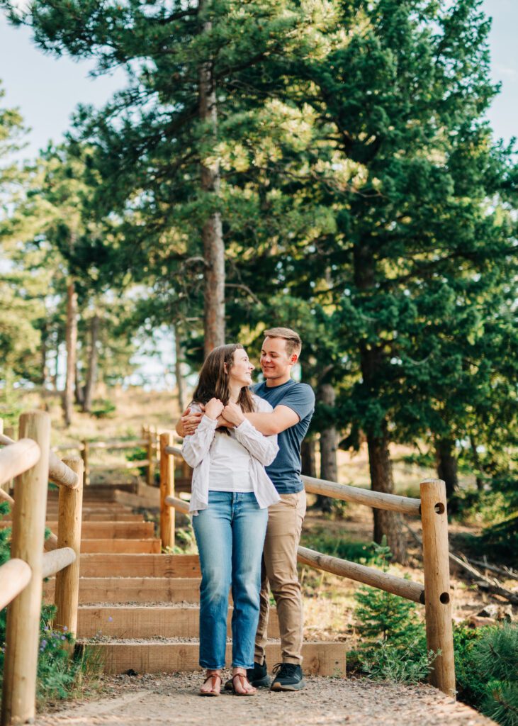 boyfriend hugging his girlfriend from behind and smiling at her in the forest during their boulder engagement session