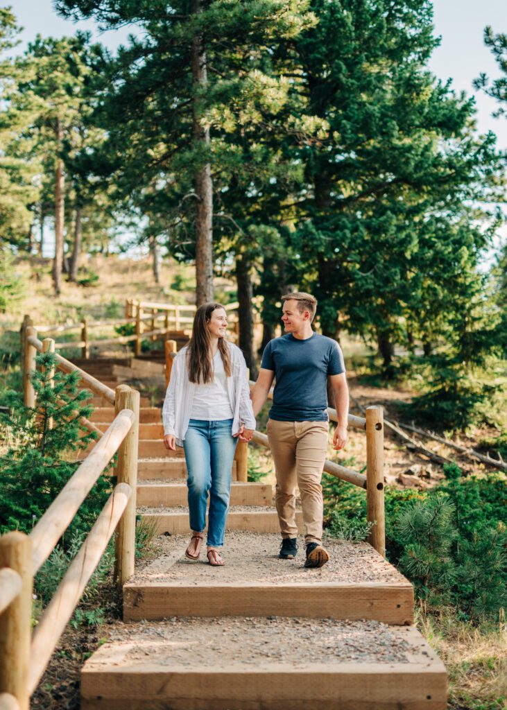 engaged couple holding hands and walking through the forest together at lost gulch overlook during their boulder colorado engagement session