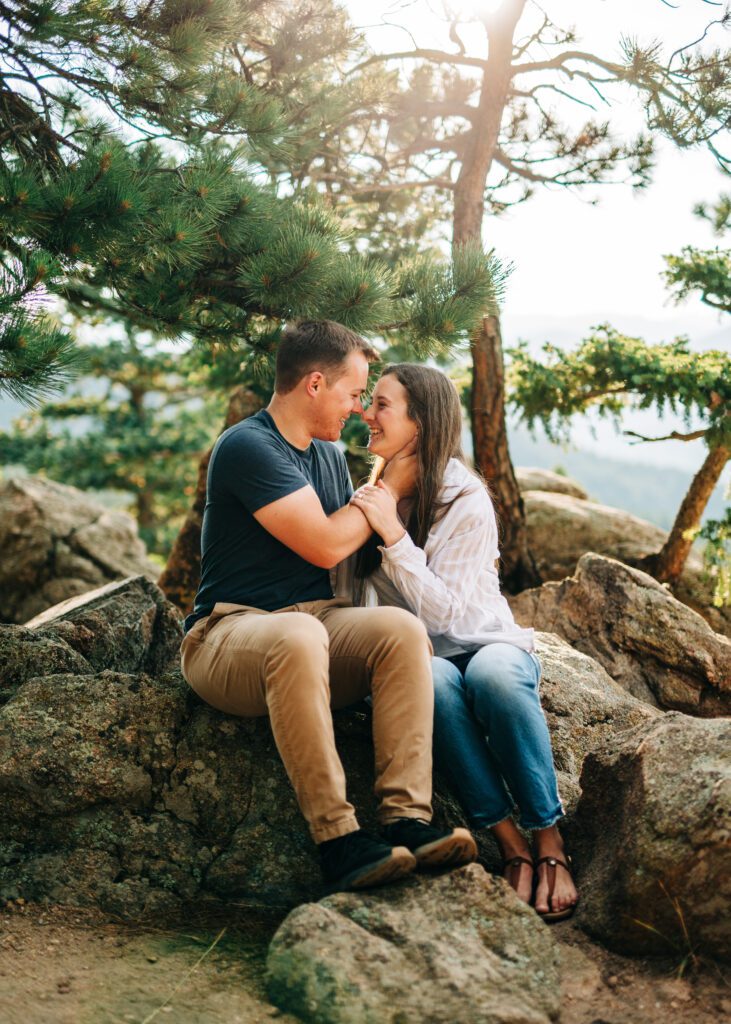 engaged couple sitting on a rock smiling at each other at lost gulch overlook in colorado during their boulder colorado engagement session