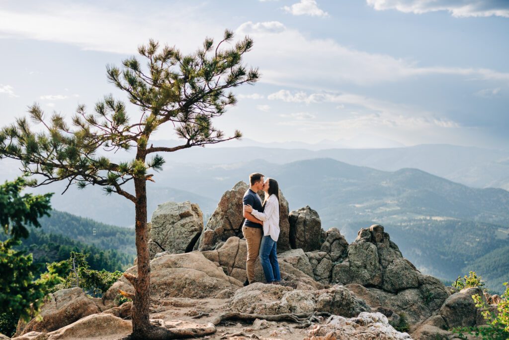 couple standing on a rocky cliff kissing during their boulder engagement photoshoot