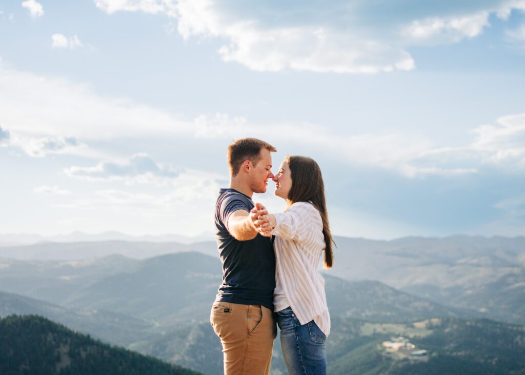 engaged couple holding hands out to the camera as they smile at eachother in the background during their boulder engagement session