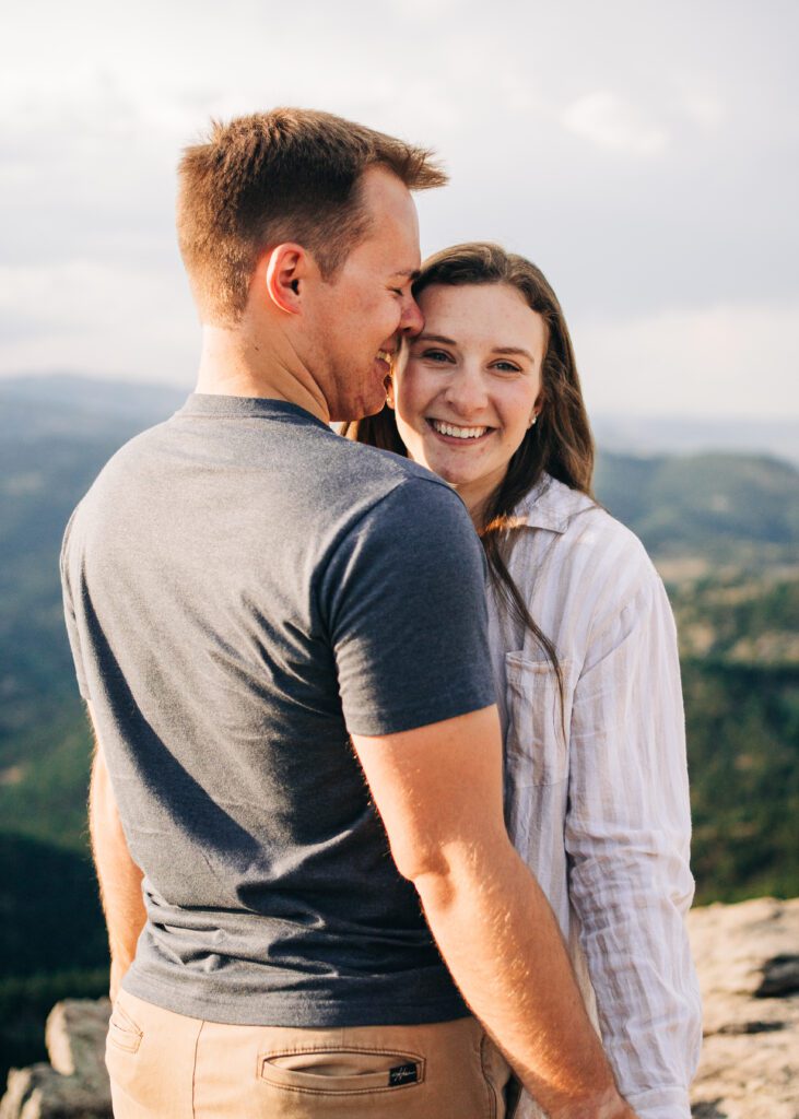 girlfriend smiling at the camera while her boyfriend kisses her temple during their boulder colorado engagement session