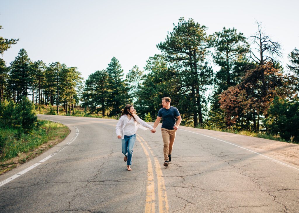 engaged couple holding hands and running down the road during the boulder engagement session