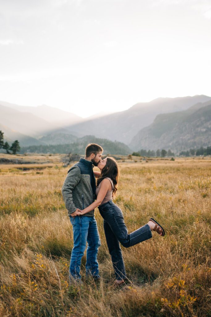 girlfriend reaching up to kiss her boyfriend during their engagement session in Rocky Mountain National Park at sunset