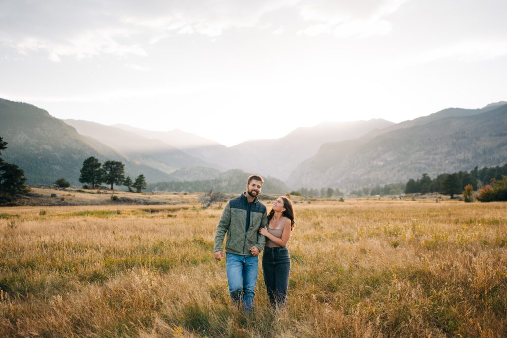 engaged couple walking together through a field after their surprise proposal in rocky mountain national park