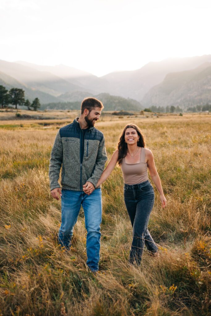 kadi smiling at the camera as her and corwin walk towards the camera during their engagement session in rocky mountain national park