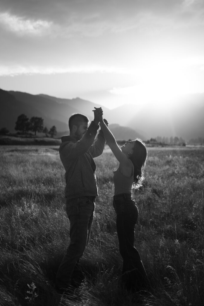 kadi and corwin holding hands above their heads smiling at each other during their engagement session in rocky mountain national park