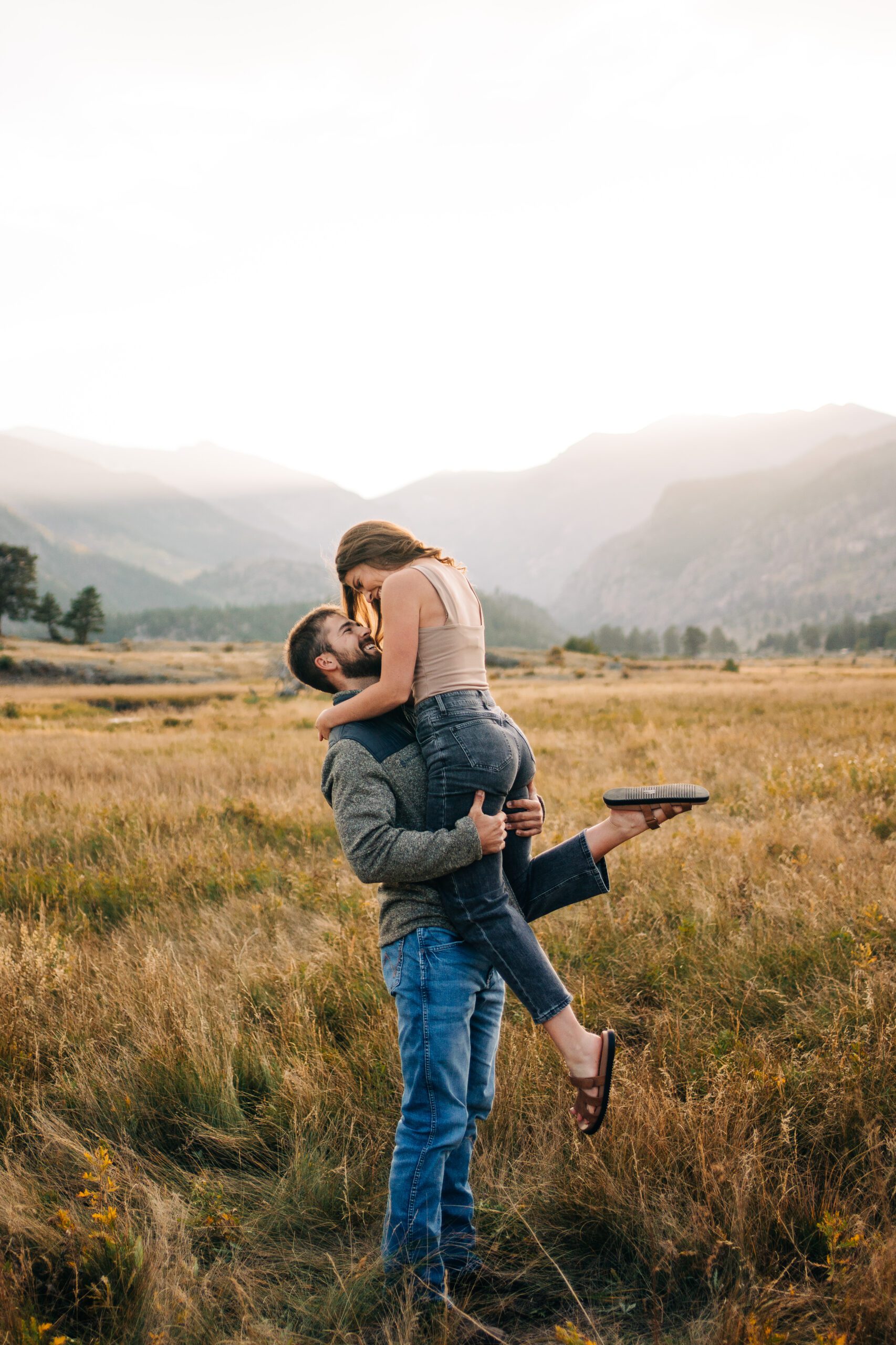 Boyfriend holding his girlfriend up while kissing her in a field at Moraine Park during their engagement session in Rocky Mountain National Park Colorado