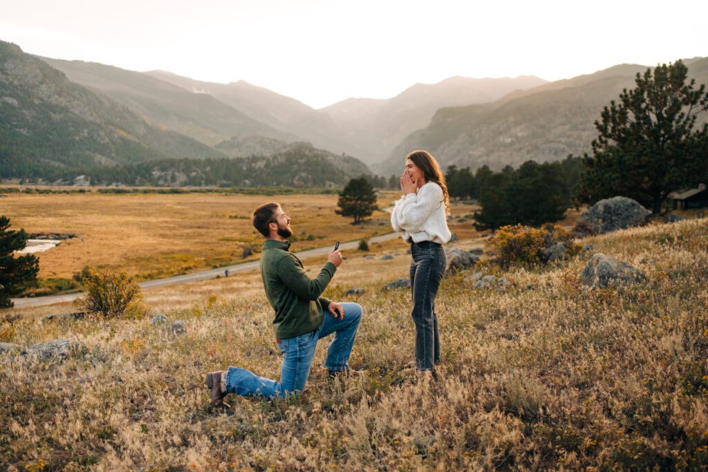 Fiance down on one knee while he proposes to his girlfriend at sunset in Moraine Park at Rocky Mountain National Park in Colorado