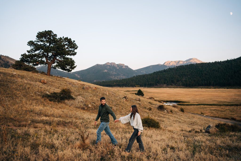 cute engaged couple walking through a field in Moraine Park at Rocky Mountain National Park