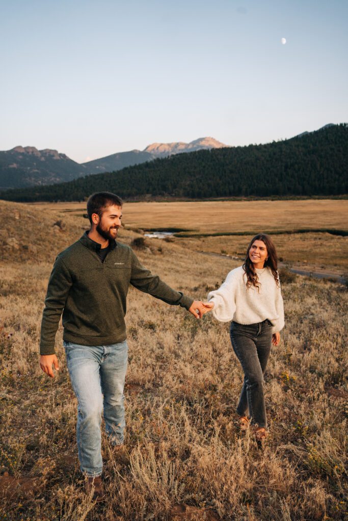 engaged couple holding hands and walking together during blue hour in rocky mountain national park