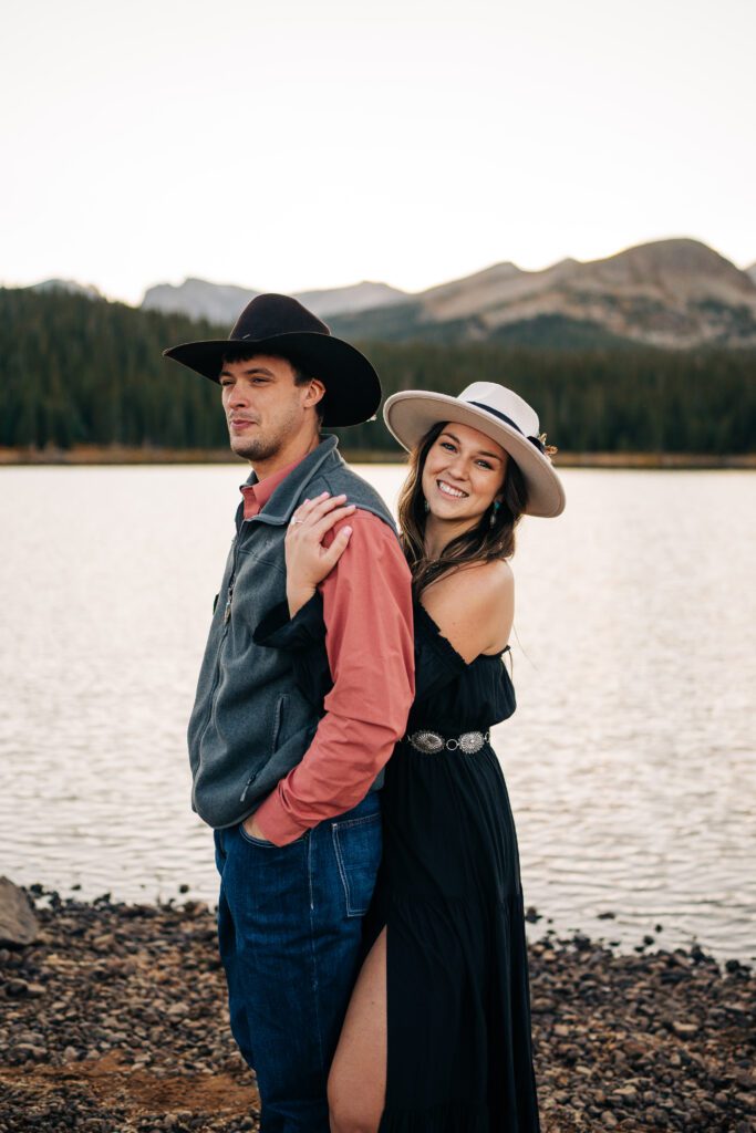 girl hugging her boyfriend from behind and smiling at the camera while he looks off in the distance during their brainard lake engagement session in Colorado