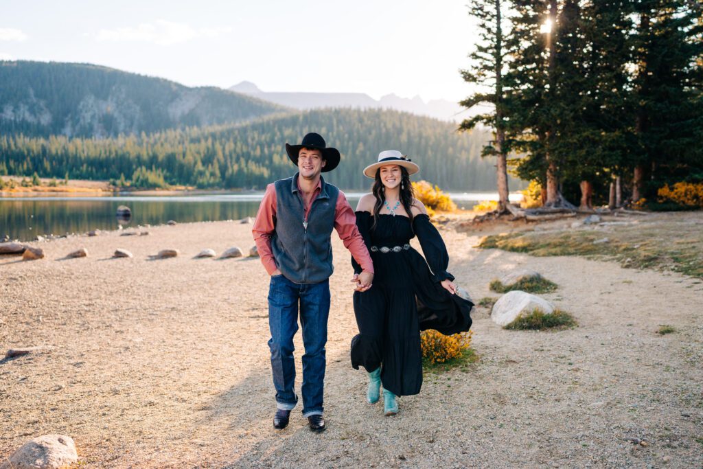 engaged couple holding hands walking along the lake side during their brainard lake engagement session in colorado
