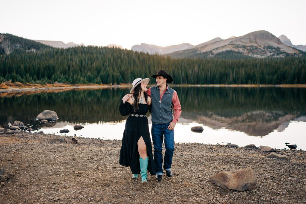 Engaged couple smiling and holding hands walking towards the camera at Brainard Lake in Colorado