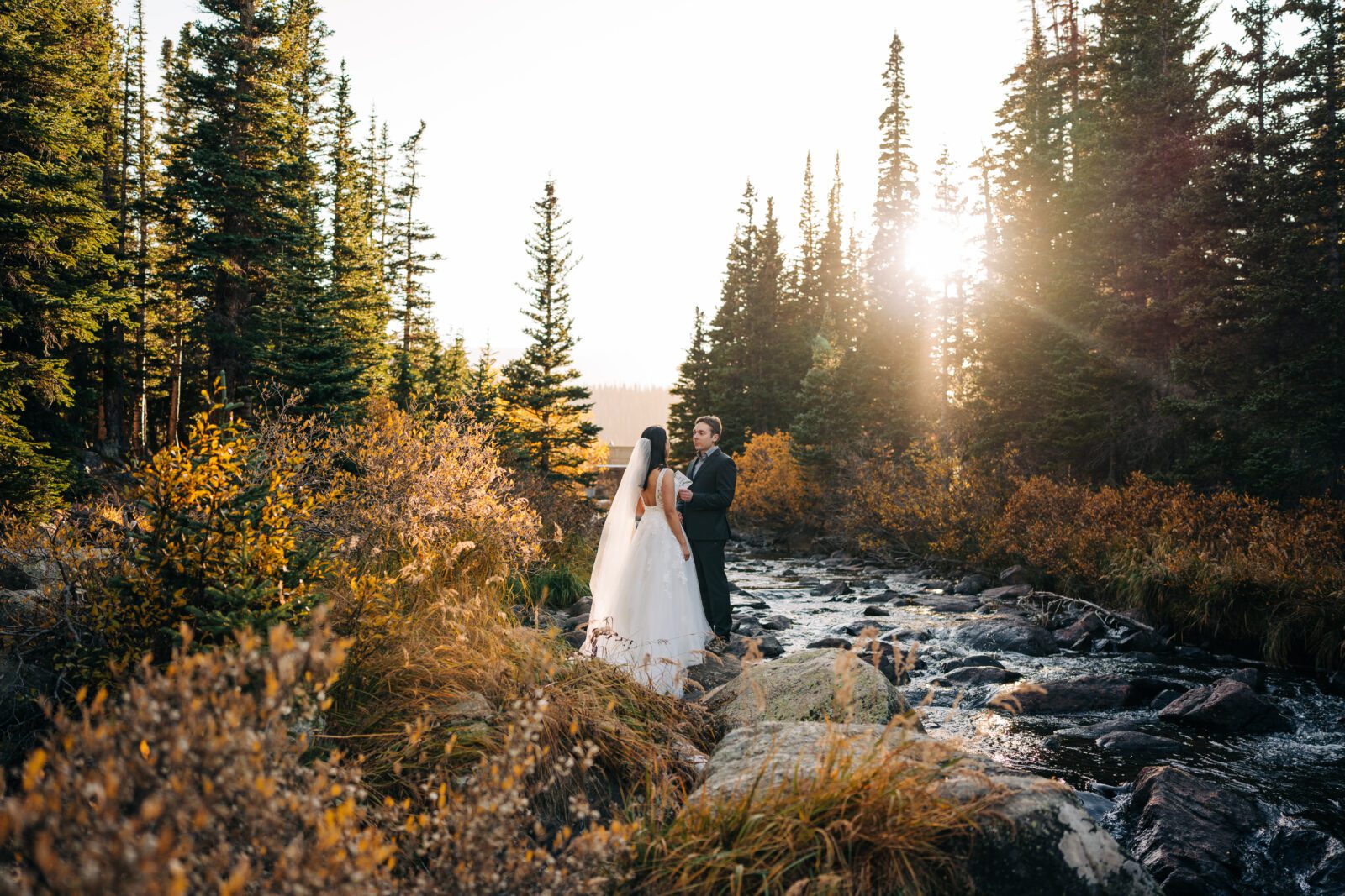 Bride and groom standing in the forest next to a river a sunset during their Brainard Lake Elopement in Colorado 