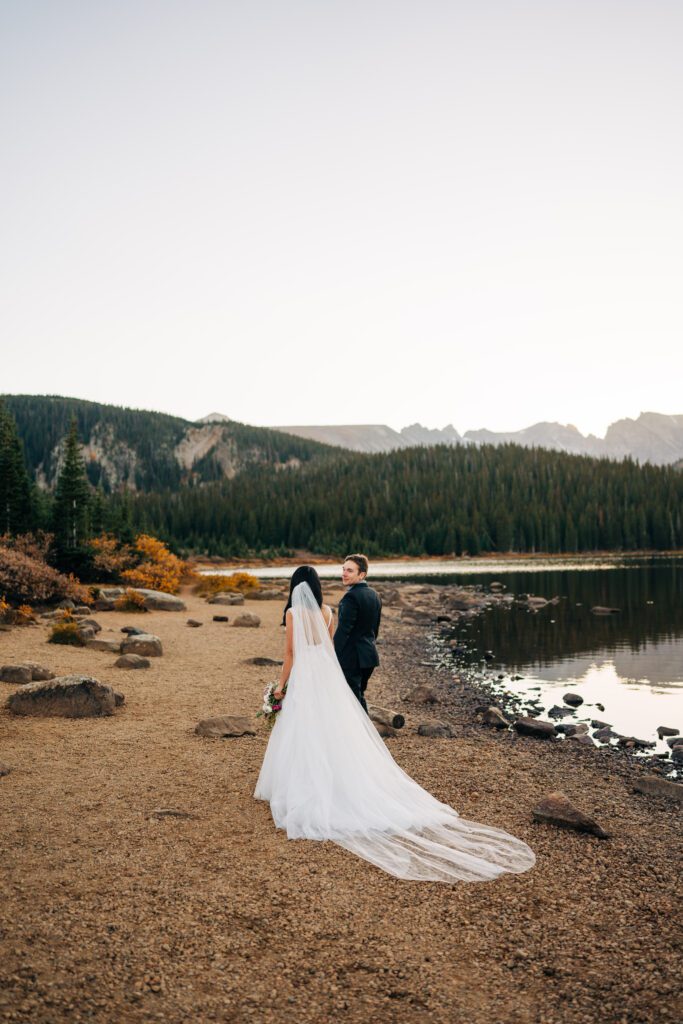 bride and groom holding hands and walking away from the camera and towards the mountains during their brainard lake elopement near boulder colorado