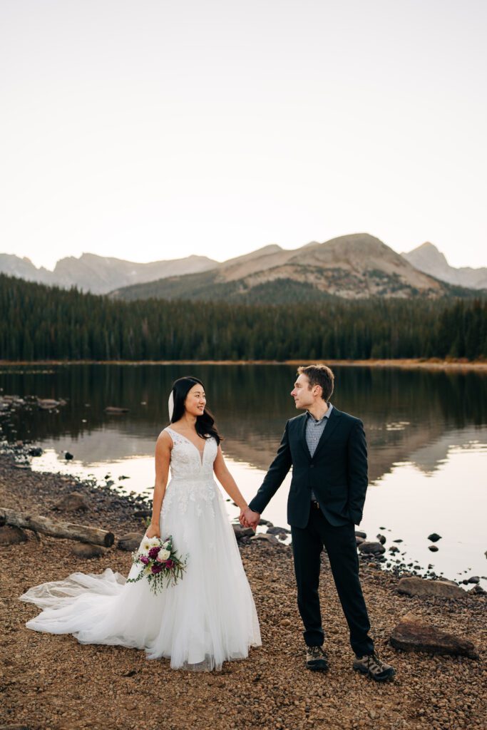 bride and groom walking along the lake smiling at eachother during their brainard lake elopement near boulder colorado