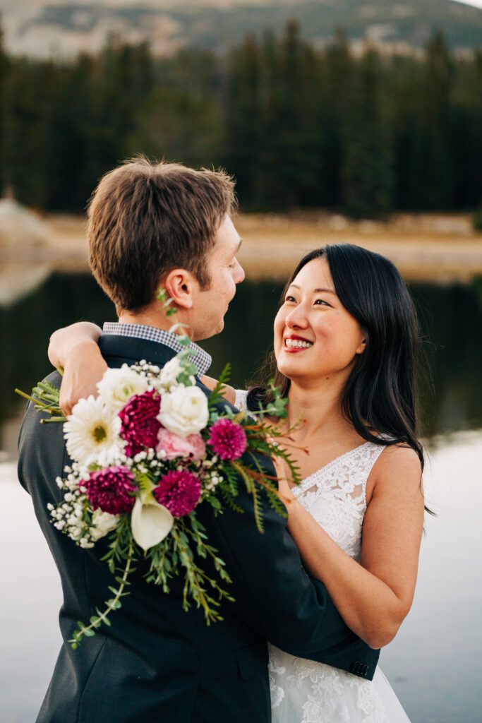 bride wrapping her arms around groom while smiling up at him while displaying her beautiful fall bouquet during their colorado elopement at brainard lake