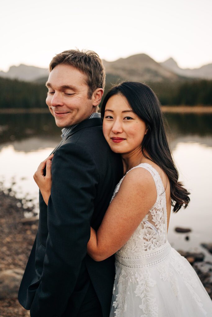 bride hugging groom from behind while smiling at the camera and him looking down at her during their brainard lake elopement near boulder colorado