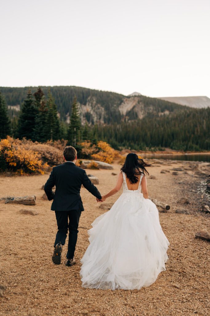 bride and groom holding hands and running away from the camera during their brainard lake elopement near boulder colorado