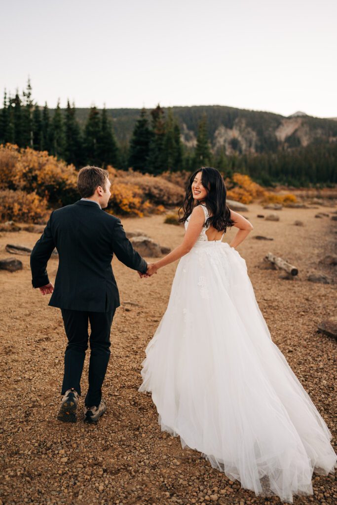 bride and groom holding hands running away from the camera while the bride looks back over her shoulder during their brainard lake elopement in colorado