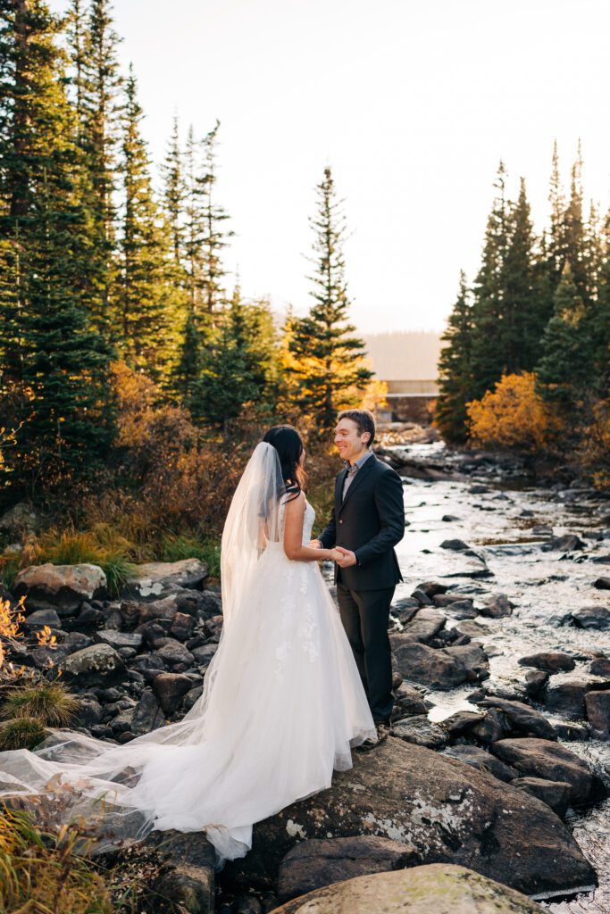 bride and groom holding hands in the forest at sunset next to a river during their brainard lake elopement