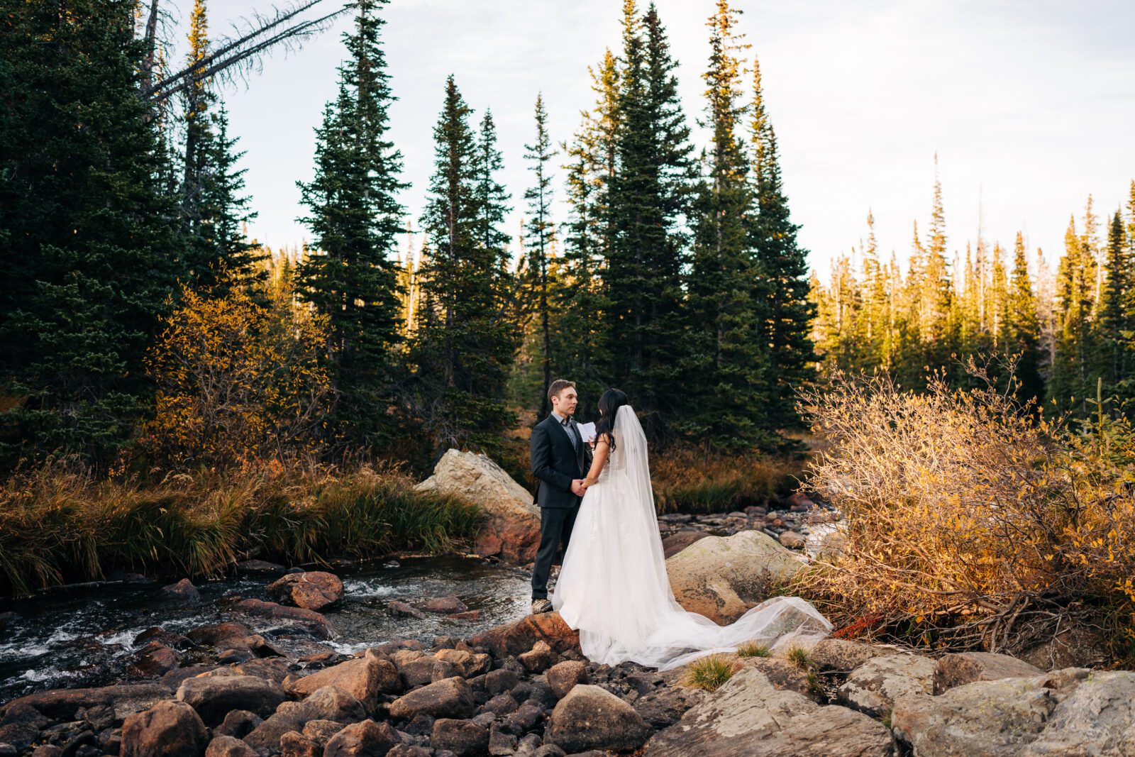 bride reading her wedding vows to the groom during their brainard lake elopement in the forest at sunset next to a river 