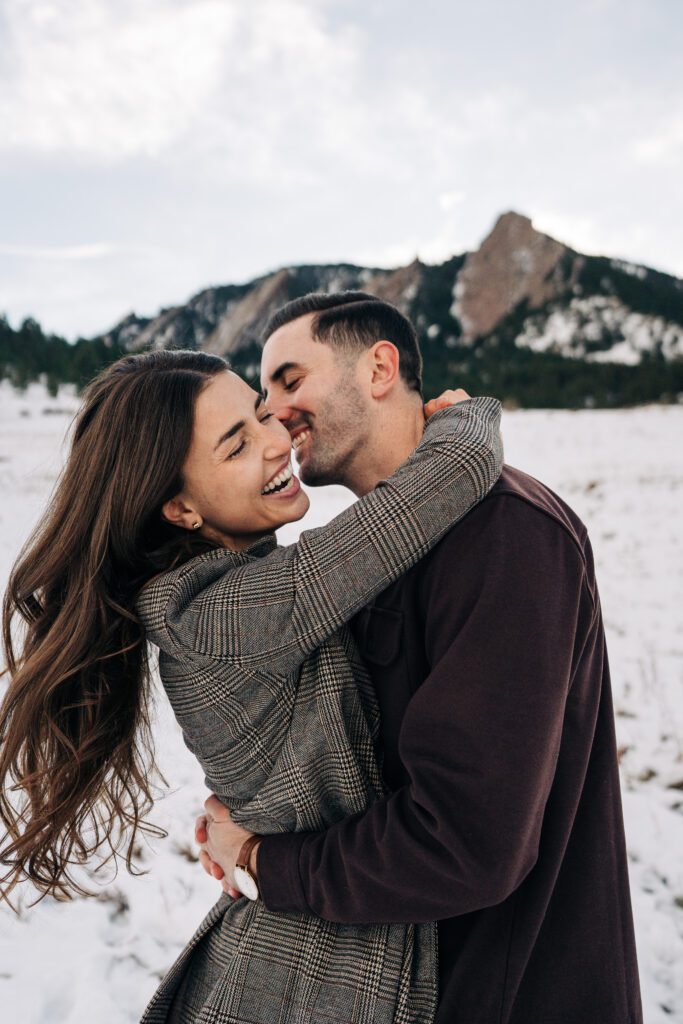 Girlfriend getting swung around by her fiance while he kisses her neck in a snowy field at the base of Chautauqua Park in Boulder, Colorado during their winter engagement photoshoot