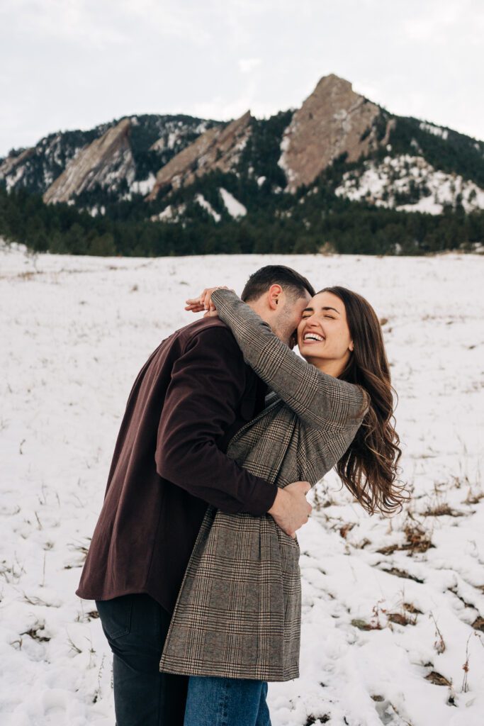 Boyfriend hugging his girlfriend and whispering something in her ear during their winter engagement session in Boulder, Colorado