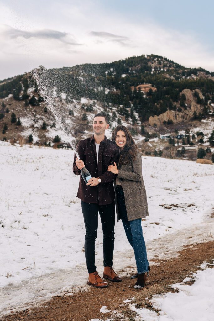 Engaged couple spraying champagne to celebrate their engagement at Chautauqua Park in Boulder, Colorado during their winter engagement session