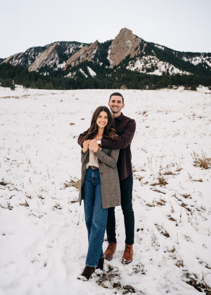 Fiance wrapping his girlfriend up in a hug in a snow field at the base of the Boulder, Colorado Flatirons during their Colorado Winter Engagement Session