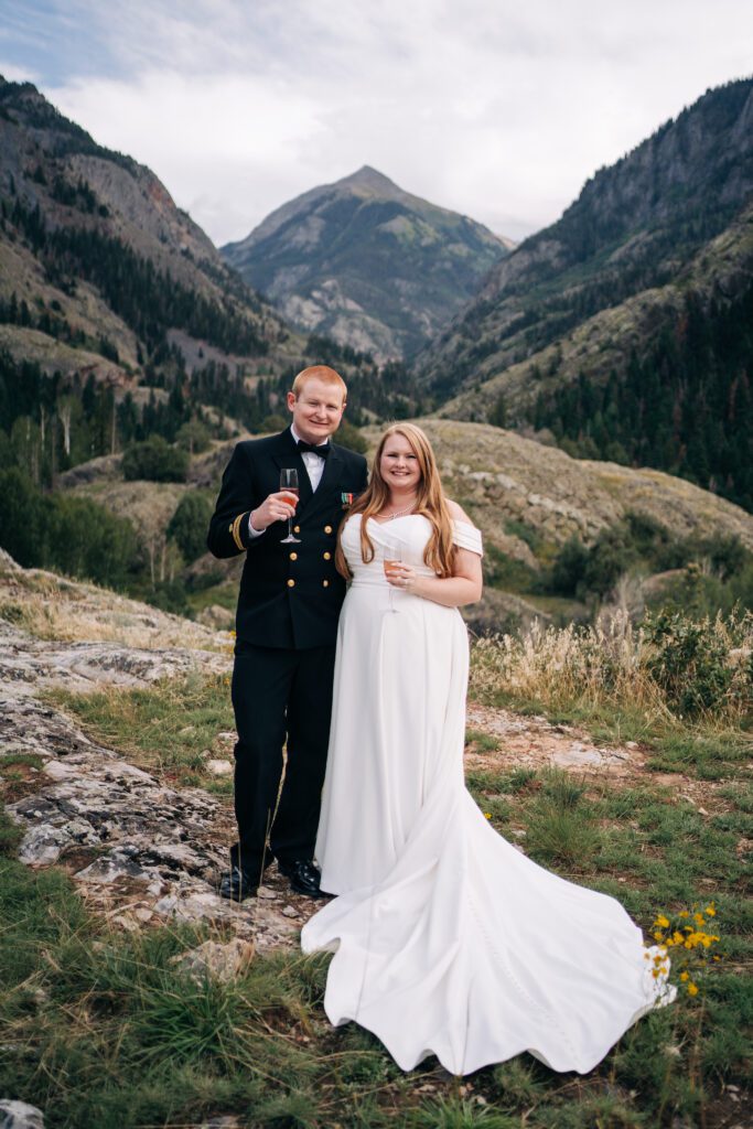 bride and groom holding a glass of champagne in front of a huge mountain peak during their ouray elopement in colorado