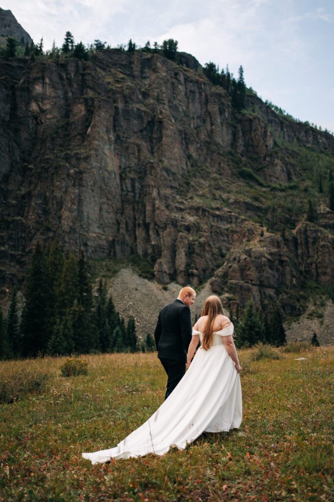 bride and groom holding hands walking through a meadow in the millon dollar highway during their ouray elopement