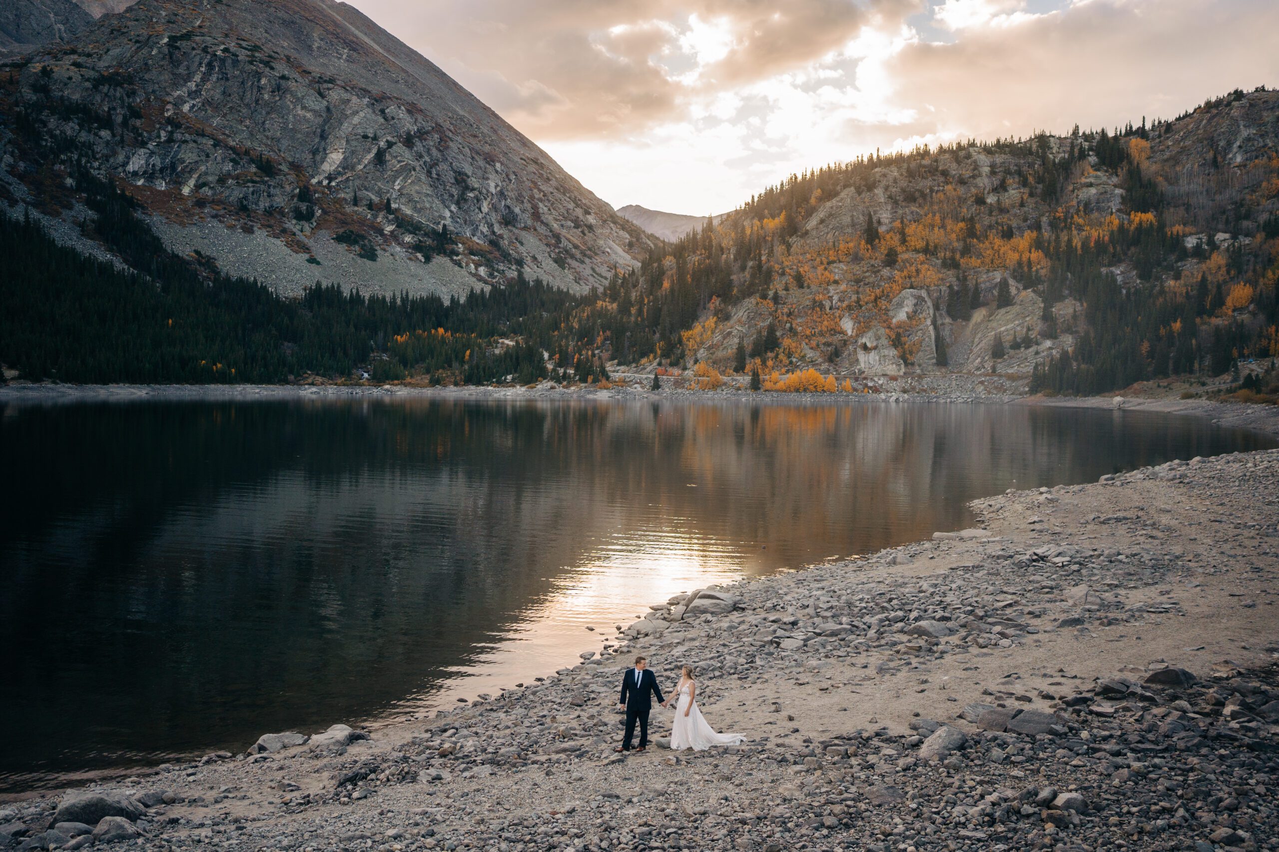 Bride and groom holding hands and walking along an alpine lake in the Colorado mountains during their Breckenridge elopement