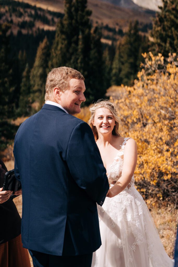 Bride holding grooms hands smiling and laughing while reading their vows during their Breckenridge elopement