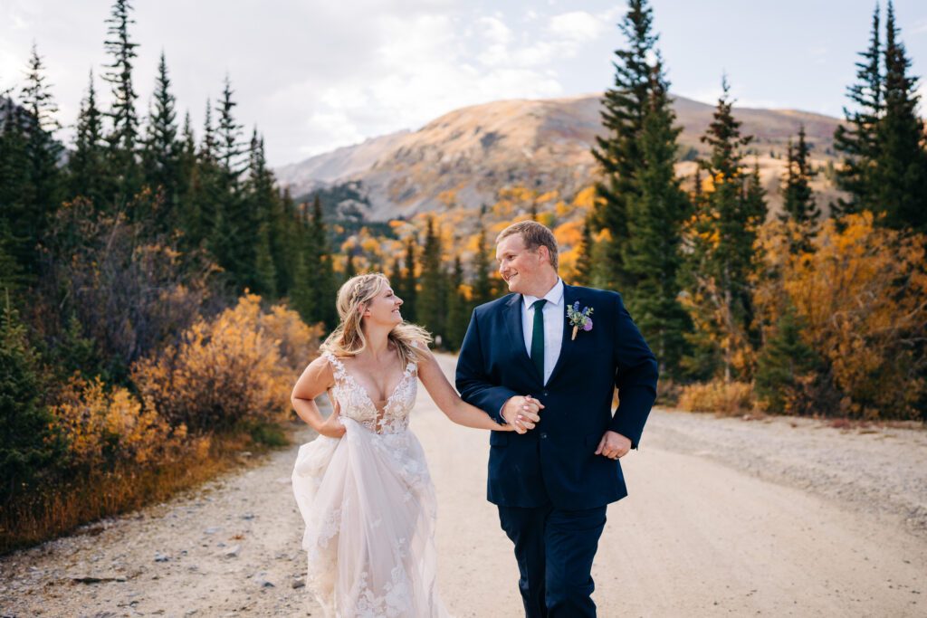 Bride and groom holding hands and running down the road in the mountains of Colorado during their Breckenridge elopement photos