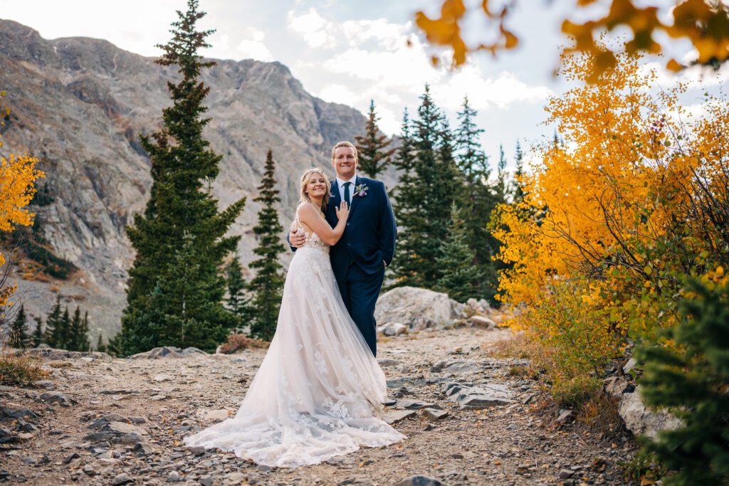 Bride and groom cuddled up on eachother as the smile at the camera on top of a mountain in Colorado during their breckenridge elopement photos