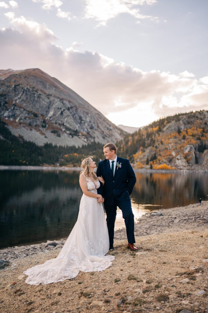 bride holding on to the grooms arm and smiling up at him on the lakeshore of a Colorado alpine lake during their Breckenridge elopement