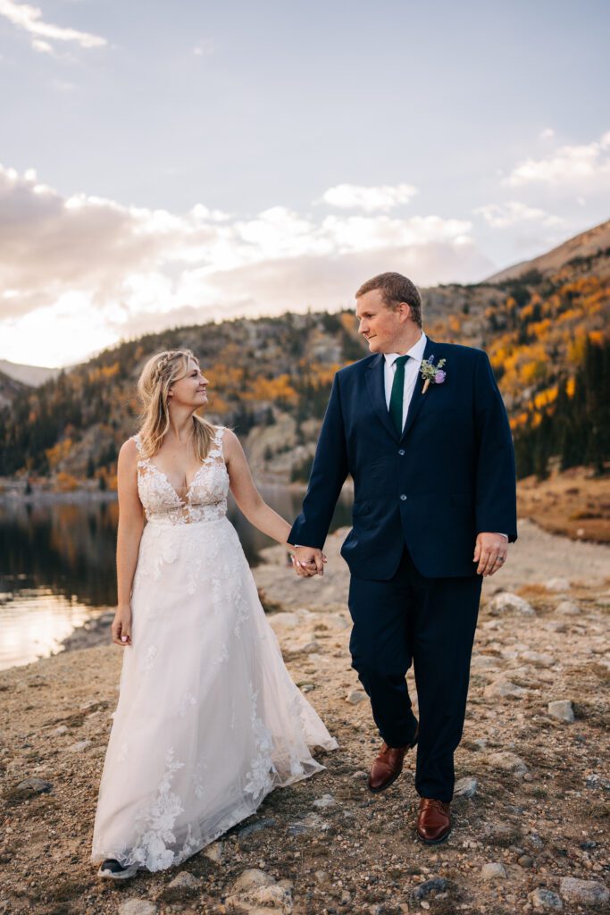 bride and groom holding hands and walking towards the camera on the shore of an alpine lake in Colorado during their Breckenridge elopement