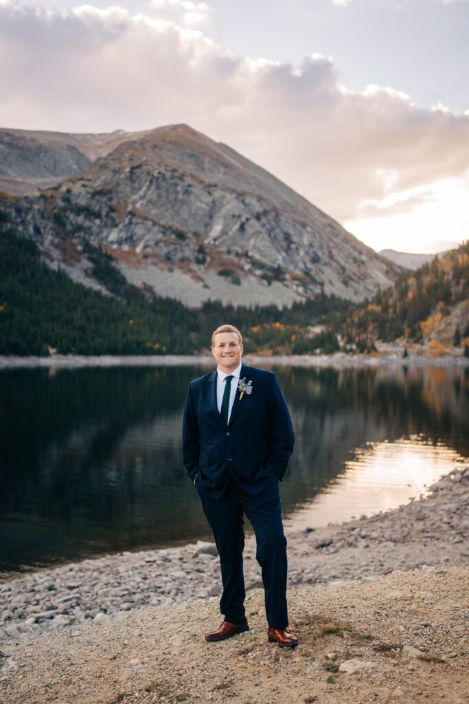 solo shot of the groom smiling at the camera on the shore of an alpine lake in Colorado during his Breckenridge elopement